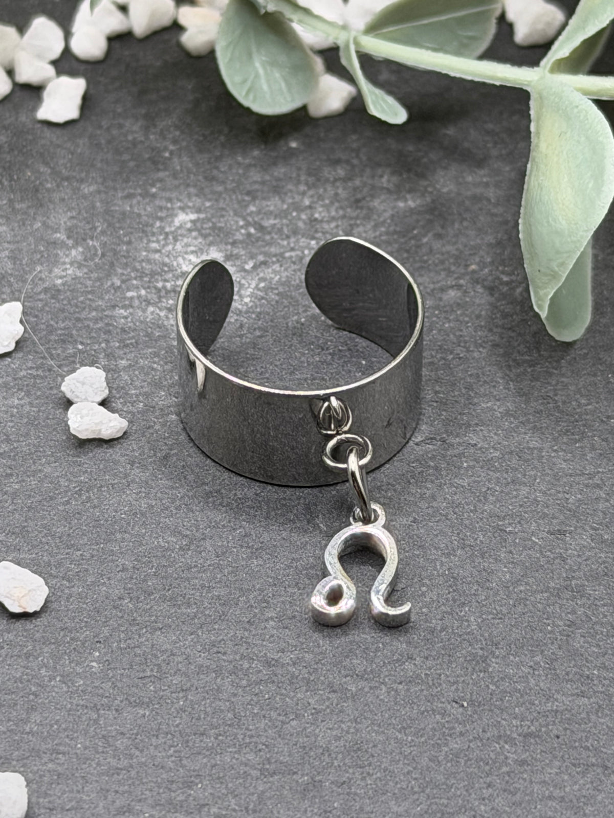 Bague Cassiopée à monture large en acier inoxydable argenté, avec une breloque du signe du Lion suspendue.