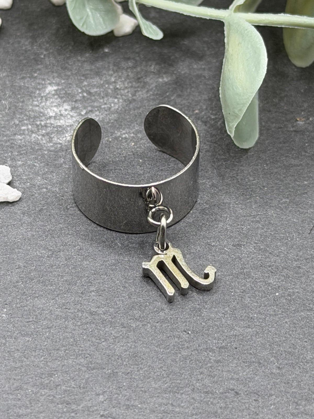 Bague Cassiopée à monture large en acier inoxydable argenté, avec une breloque du signe du Scorpion suspendue.