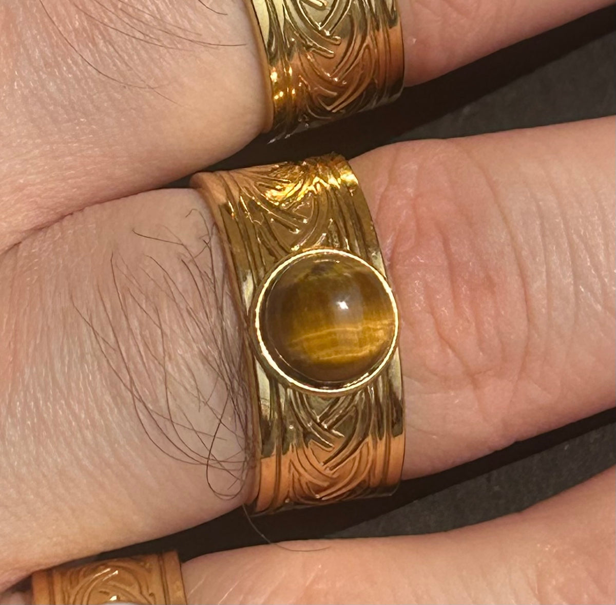 Bague Sylmor en acier inoxydable doré avec cabochon rond en œil de tigre brun doré, portée au doigt.