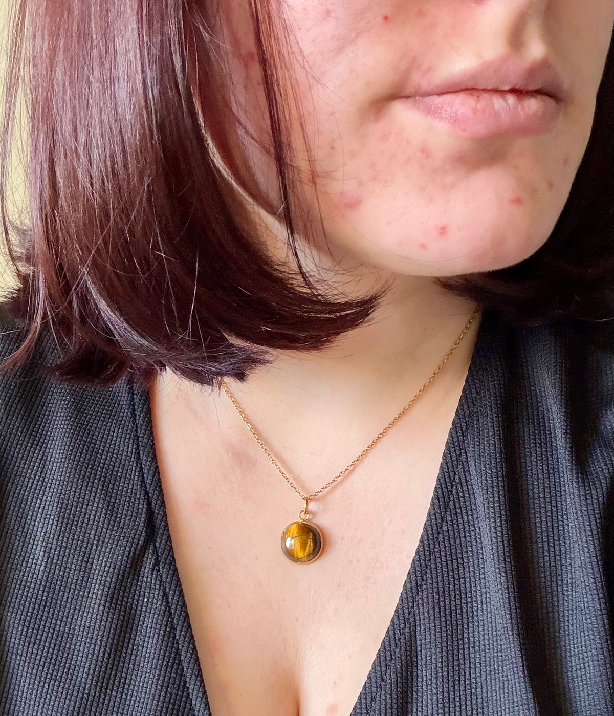 Gros plan du collier Séléna porté, en acier inoxydable doré, avec pendentif rond en œil de tigre sur un haut noir.