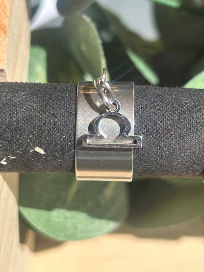 Bague Cassiopée à monture large en acier inoxydable argenté, avec une breloque du signe de la Balance suspendue.