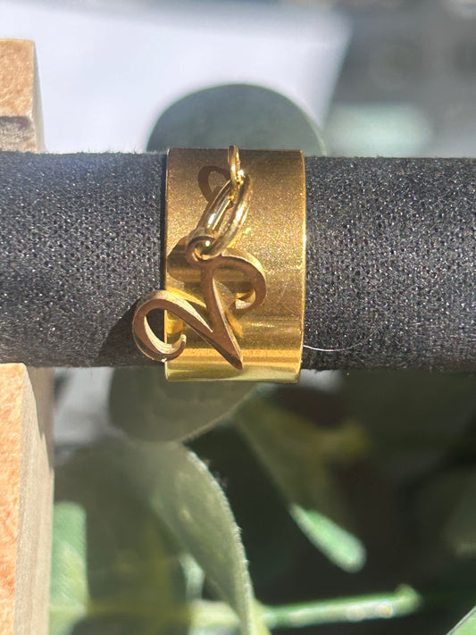 Bague Cassiopée à monture large en acier inoxydable doré, avec une breloque du signe du Bélier suspendue.