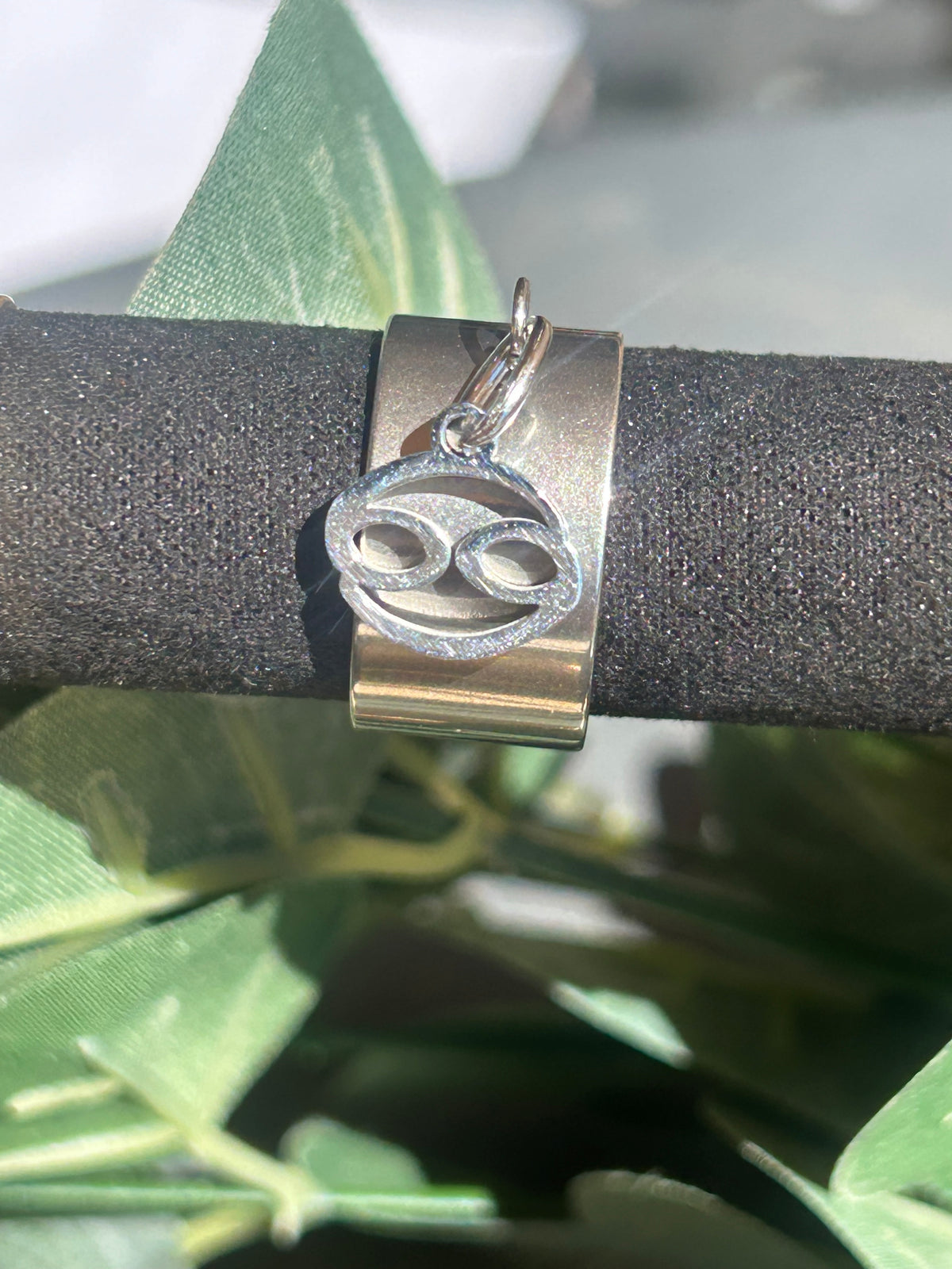 Bague Cassiopée à monture large en acier inoxydable argenté, avec une breloque du signe du Cancer suspendue.