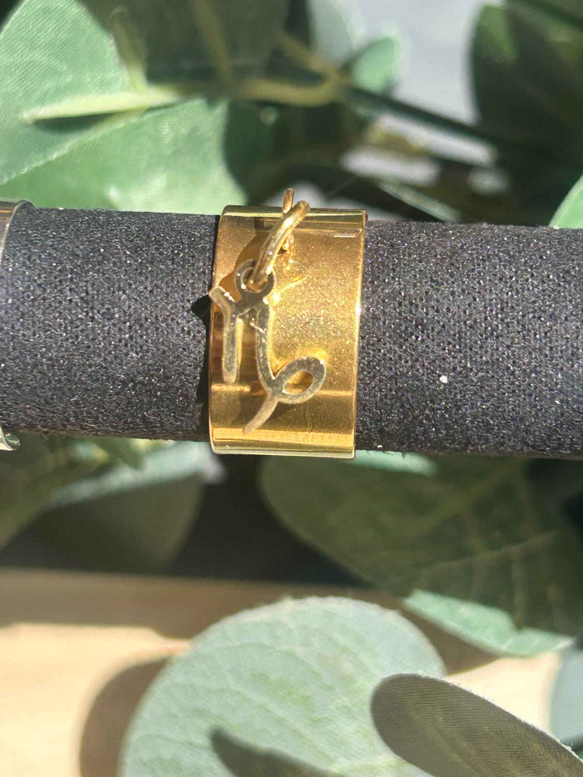 Bague Cassiopée à monture large en acier inoxydable doré, avec une breloque du signe du Capricorne suspendue.