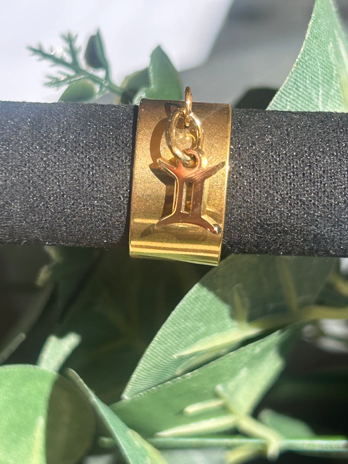 Bague Cassiopée à monture large en acier inoxydable doré, avec une breloque du signe des Gémeaux suspendue.