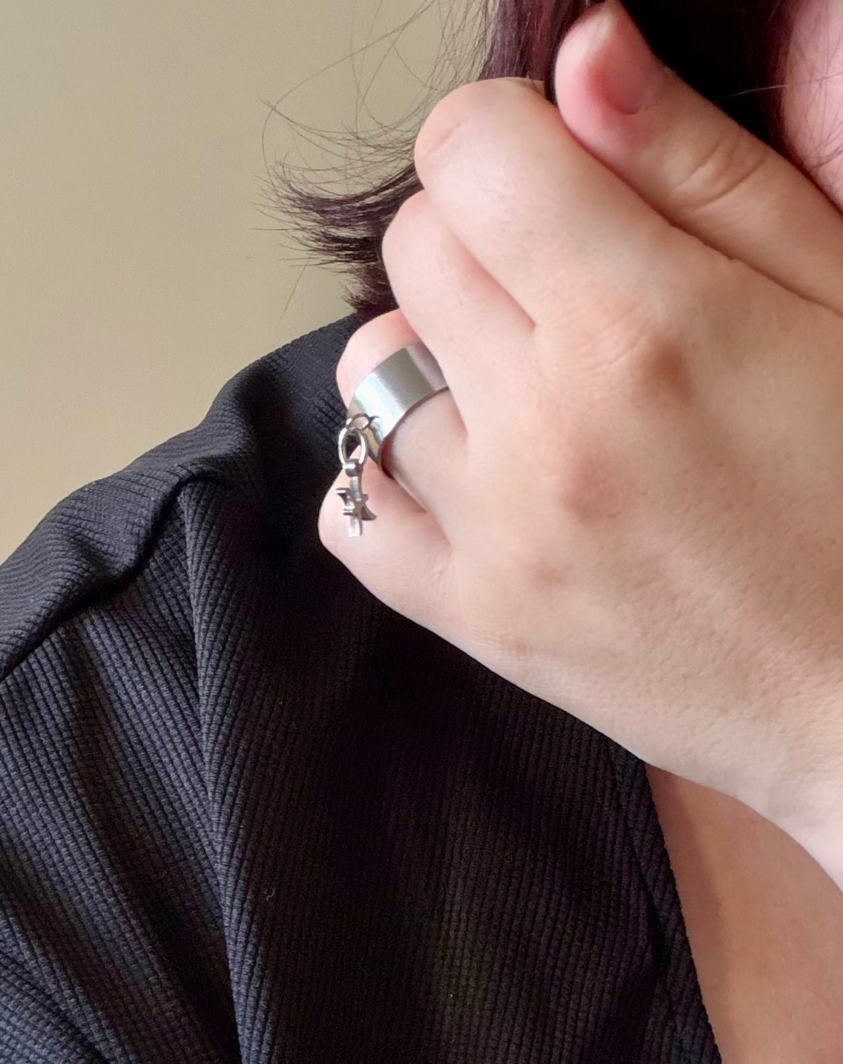 Bague Cassiopée portée à la main, avec une monture large en acier inoxydable argenté et une breloque du signe des Poissons suspendue.