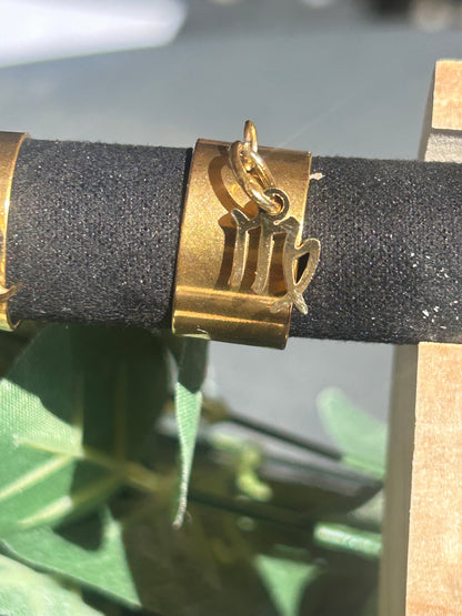 Bague Cassiopée à monture large en acier inoxydable doré, avec une breloque du signe de la Vierge suspendue.