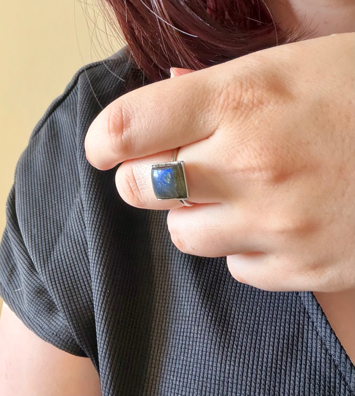 Bague Kaora réglable portée à la main, en acier inoxydable argenté avec un cabochon carré en labradorite aux reflets bleus.