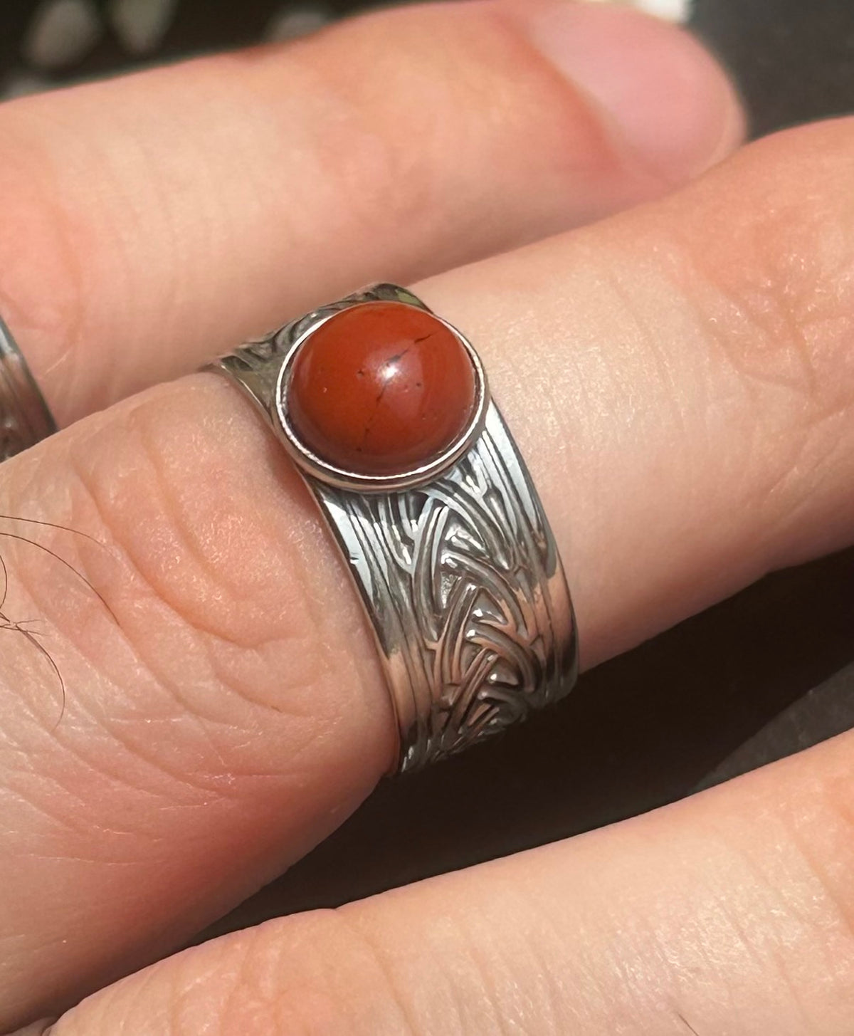 Bague Sylmor en acier inoxydable argenté avec cabochon rond en jaspe rouge, portée au doigt.