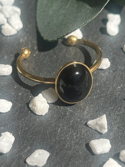 Bague Thémis réglable en acier inoxydable doré, ornée d’un cabochon ovale en agate noire.