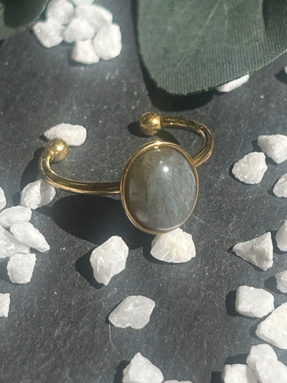 Bague Thémis réglable en acier inoxydable doré, ornée d’un cabochon ovale en labradorite aux nuances grises.