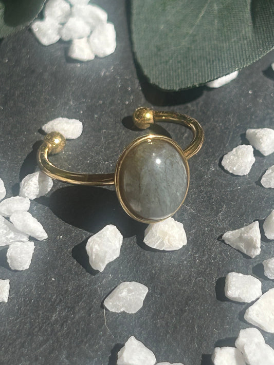 Bague Thémis réglable en acier inoxydable doré, ornée d’un cabochon ovale en labradorite aux nuances grises.