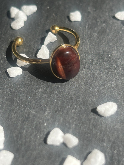 Bague Thémis réglable en acier inoxydable doré, ornée d’un cabochon ovale en œil de taureau aux nuances rouge brun.
