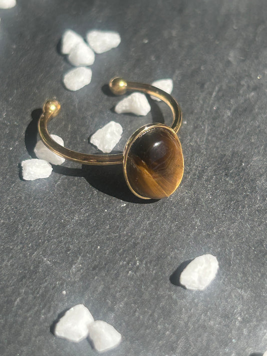 Bague Thémis réglable en acier inoxydable doré, ornée d’un cabochon ovale en œil de tigre brun doré.