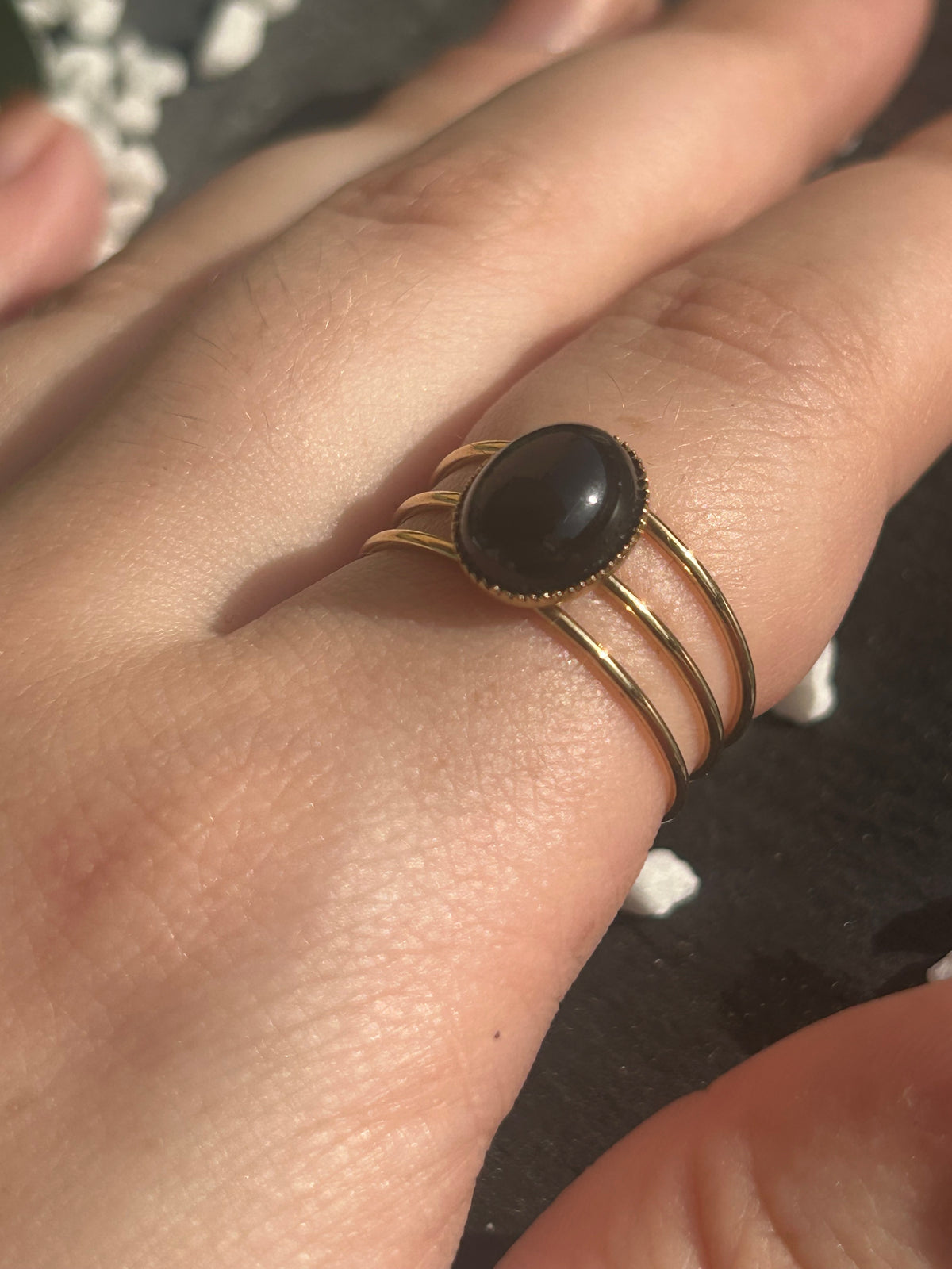 Bague Trinæa à trois anneaux en acier inoxydable doré et agate noire ovale, portée au doigt.