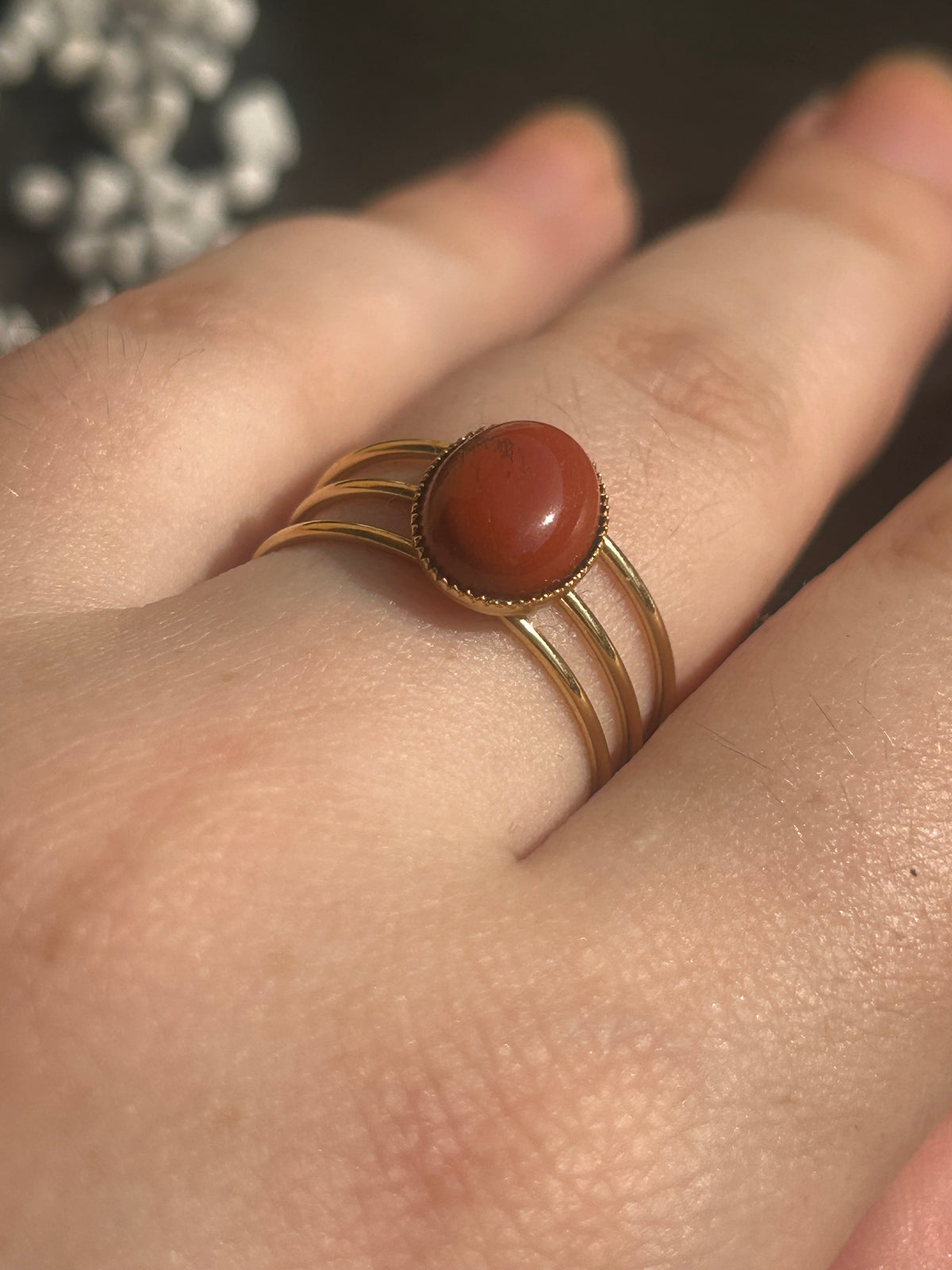 Bague Trinæa à trois anneaux en acier inoxydable doré et jaspe rouge ovale, portée au doigt.
