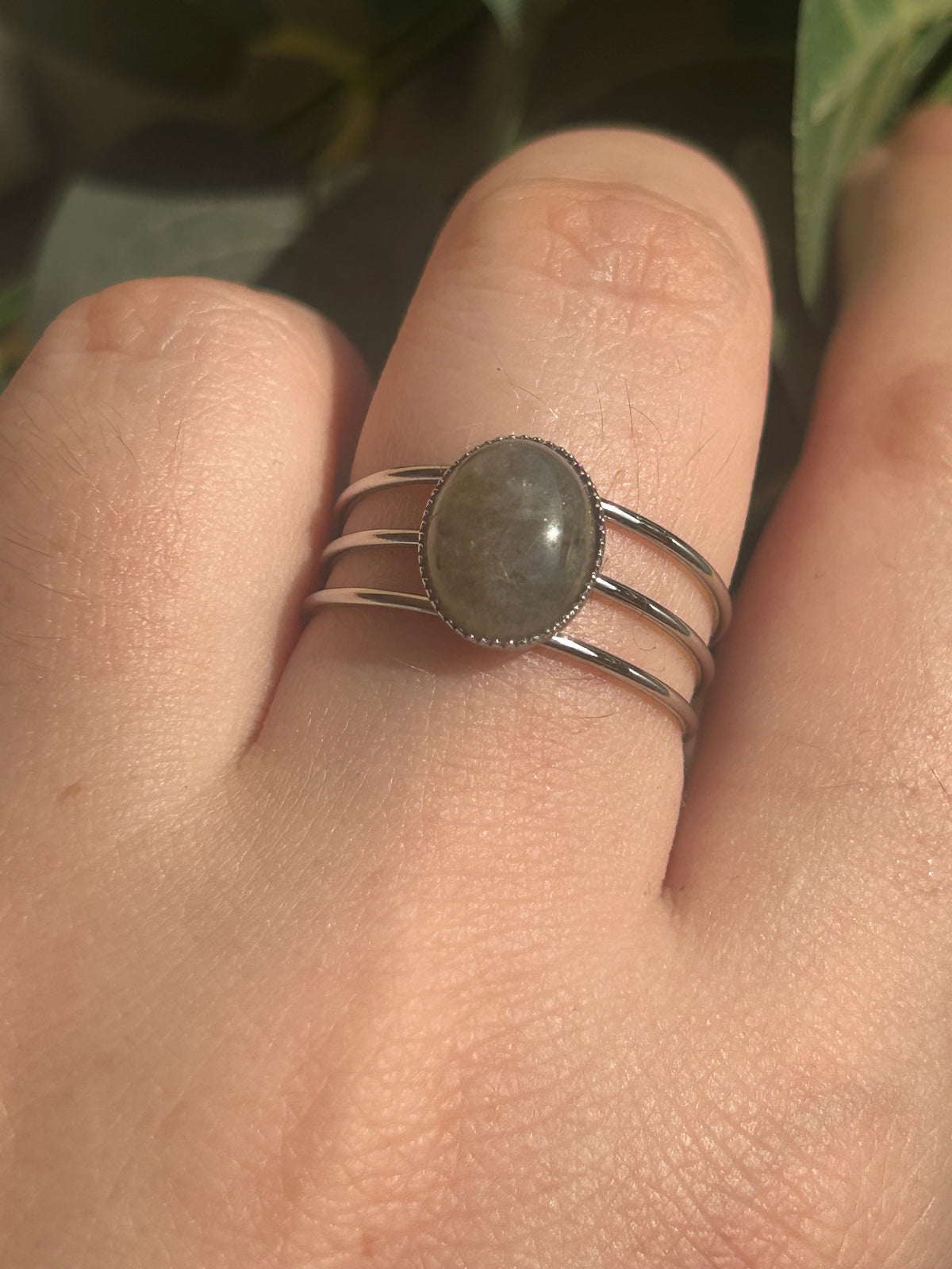 Bague Trinæa à trois anneaux en acier inoxydable argenté et labradorite ovale, portée au doigt.