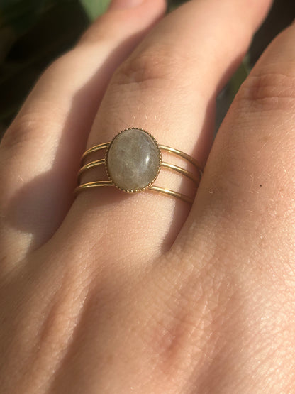 Bague Trinæa à trois anneaux en acier inoxydable doré et labradorite ovale, portée au doigt.