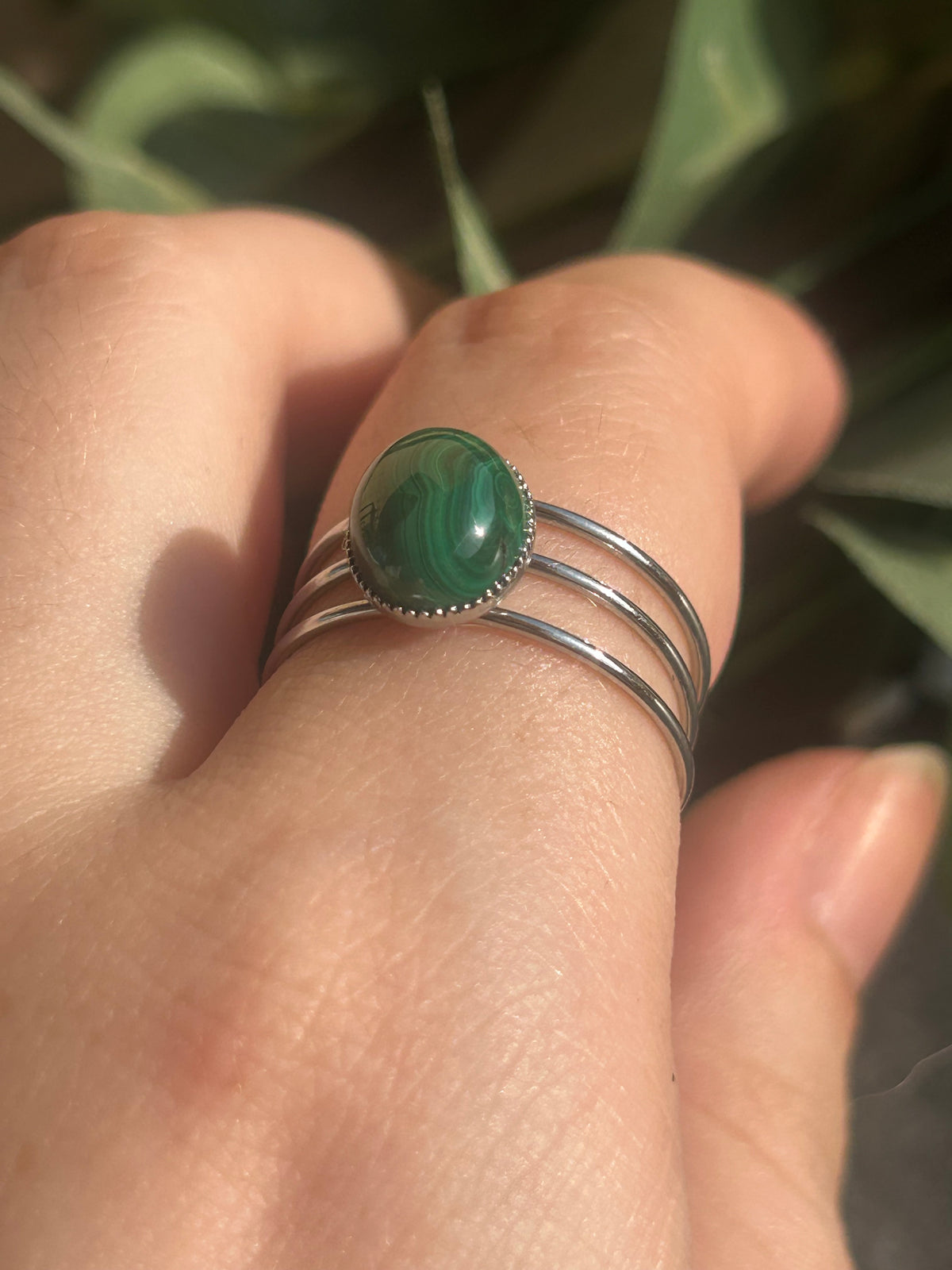 Bague Trinæa à trois anneaux en acier inoxydable argenté et malachite ovale aux motifs verts, portée au doigt.