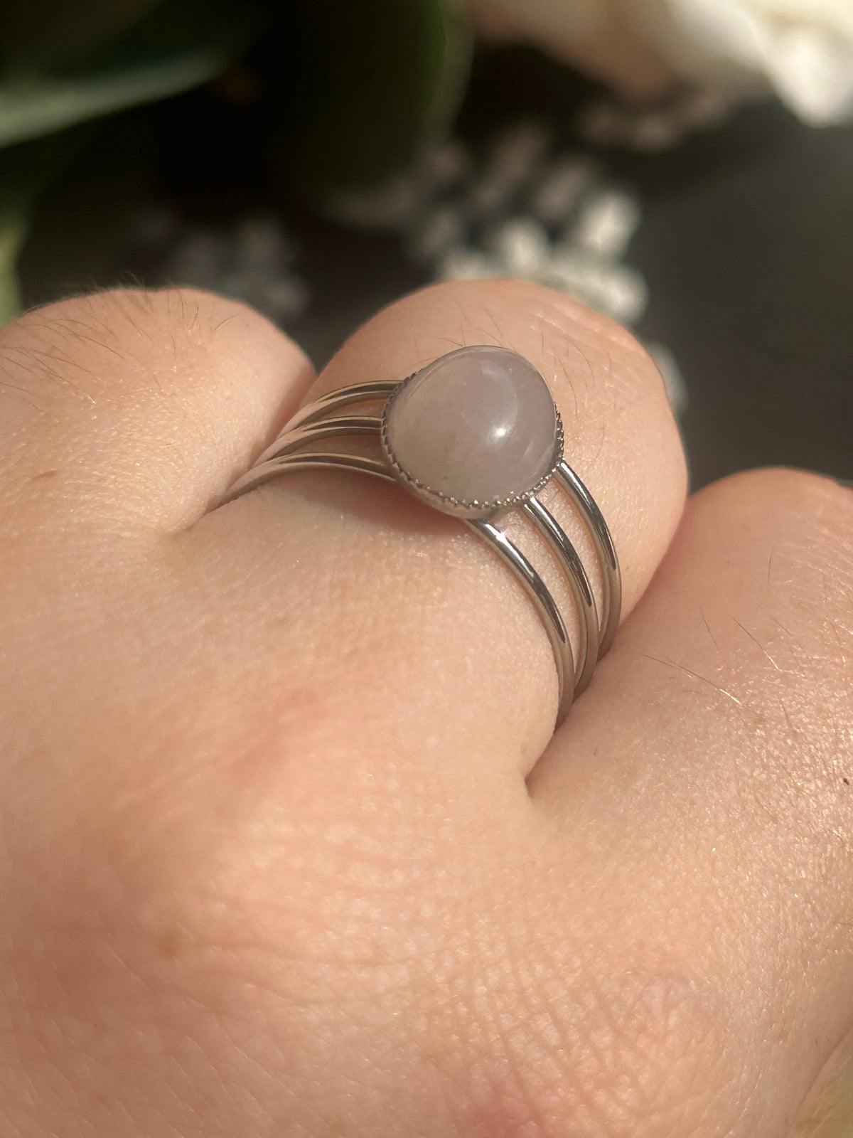 Bague Trinæa à trois anneaux en acier inoxydable argenté et quartz rose ovale, portée au doigt.