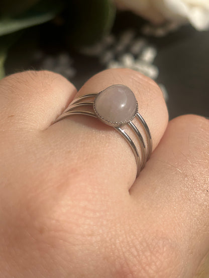 Bague Trinæa à trois anneaux en acier inoxydable argenté et quartz rose ovale, portée au doigt.