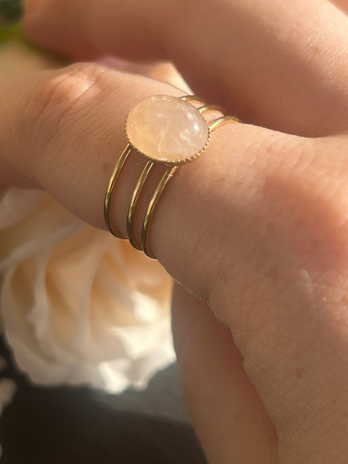 Bague Trinæa à trois anneaux en acier inoxydable doré et quartz rose ovale, portée au doigt.