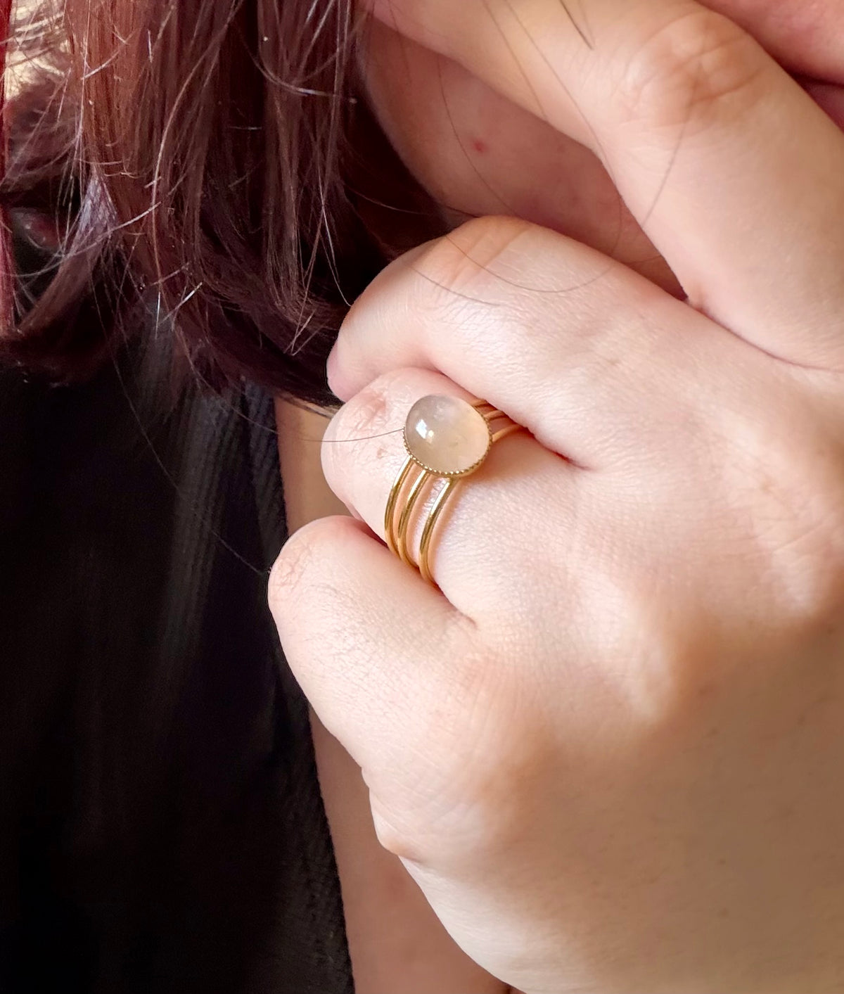 Bague Trinæa à trois anneaux en acier inoxydable doré et quartz rose ovale, portée au doigt.