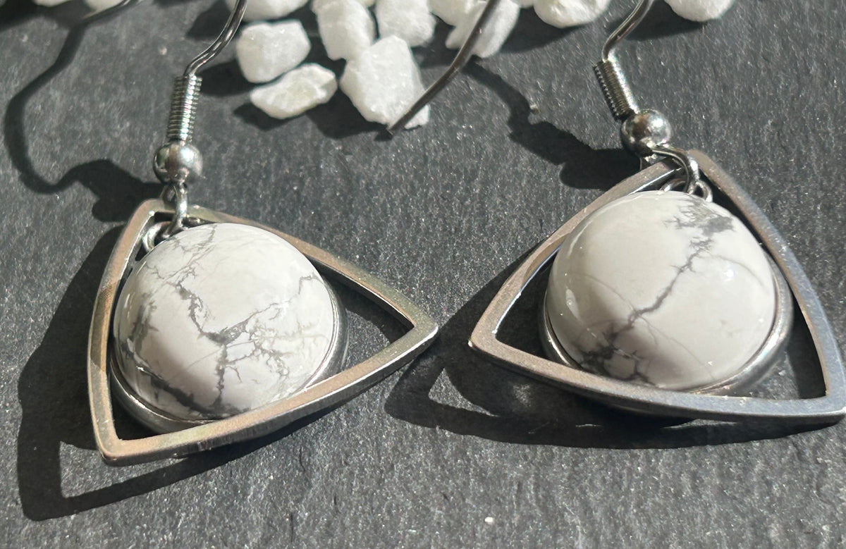 Paire de boucles d’oreilles pendantes Aeltria en acier inoxydable argenté, avec des montures triangulaires et des cabochons ronds en howlite blanche veinée de gris.