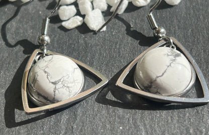 Paire de boucles d’oreilles pendantes Aeltria en acier inoxydable argenté, avec des montures triangulaires et des cabochons ronds en howlite blanche veinée de gris.