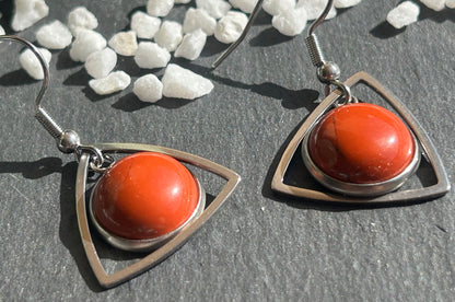 Paire de boucles d’oreilles pendantes Aeltria en acier inoxydable argenté, avec des montures triangulaires et des cabochons ronds en jaspe rouge.