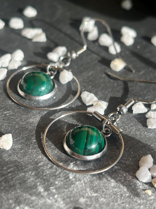 Paire de boucles d’oreilles pendantes Célestia en acier inoxydable argenté, avec des montures circulaires et des cabochons ronds en malachite verte aux motifs rubanés.