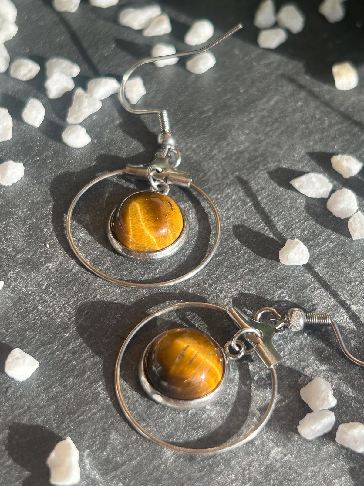 Paire de boucles d’oreilles pendantes Célestia en acier inoxydable argenté, avec des montures circulaires et des cabochons ronds en œil de tigre brun doré.