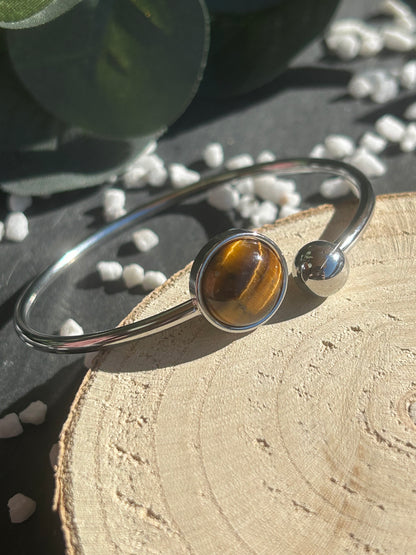 Bracelet jonc Lunae en acier inoxydable argenté, orné d’un cabochon rond de 12 mm en œil de tigre brun doré et d’une bille fixe.