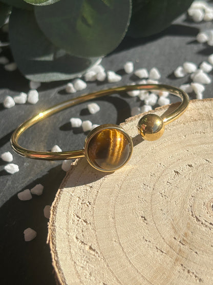 Bracelet jonc Lunae en acier inoxydable doré, orné d’un cabochon rond de 12 mm en œil de tigre brun doré et d’une bille fixe.