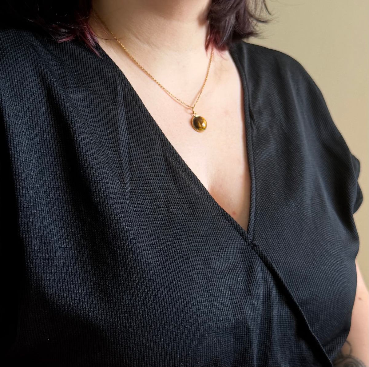 Vue d’ensemble du collier Séléna porté sur une tenue noire, avec chaîne dorée et pendentif rond en œil de tigre.